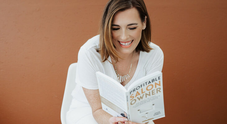 Smiling lady reading a book called Profitable Salon Owner